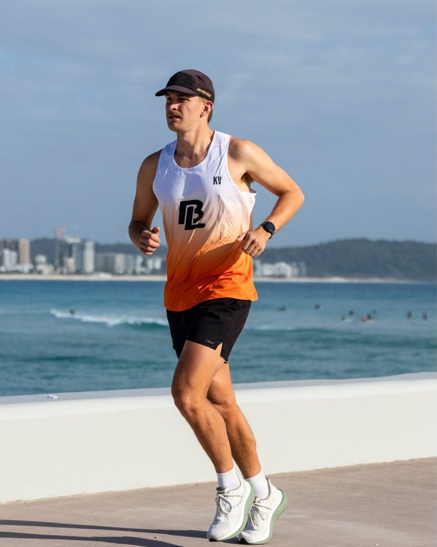 Toby running on the seafront in the white-to-orange Beyond Limits race singlet, BL logo on the chest
